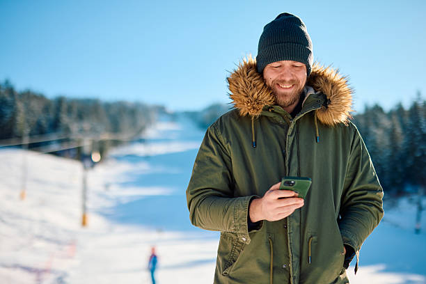 istock Smiling tourist using phone on ski slope during winter holidays 2229187770