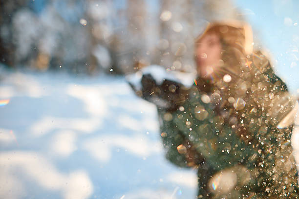 Young woman blowing snow in a serene winter forest, creating a magical scene filled with sparkling snowflakes and a dreamy, blurred effect, capturing the essence of the season