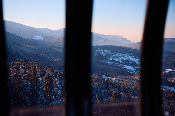 The breathtaking vista of a snow-dusted mountain range at sunset, observed through the gaps of a railing, evokes a sense of tranquility and awe