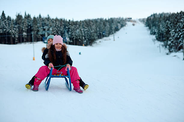 A child stands frozen on a sled at the top of a snowy hill, looking forward to the joyful fun. A child enjoys sledding in the backyard on a winter day. The concept of a child enjoying winter..