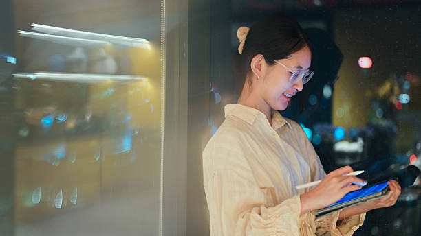 istock Asian young woman using smartphone against city skyline backdrop  future connection and human-ai interaction  in mobile experience with night cityscape, blending urban lifestyle and ai-powered apps 2229189172