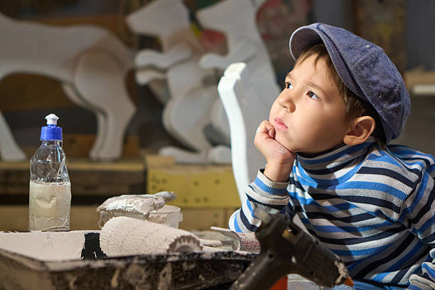 Cute preschool age boy is working in a domestic workroom repairing and restoring toy figurines of forest animals for Christmas decor. Shooting in home workshop