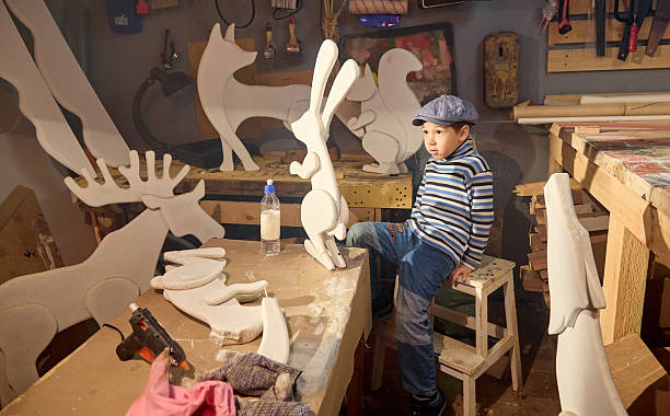 istock Diligent little boy glues ear while repairing Christmas bunny figurine in home workshop 2229192420