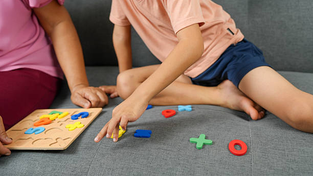 Engaging in playful learning activity, child interacts with colorful alphabet and number puzzle pieces on soft gray couch, while adult assists nearby. scene captures moment of joy and education