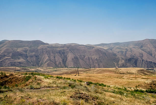 Panoramic view of arid mountain range and grasslands under clear blue sky.