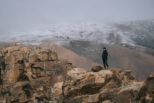 istock Mongolian Woman Standing on Rocky Cliff Overlooking Snow-Covered Mountain 2229194127