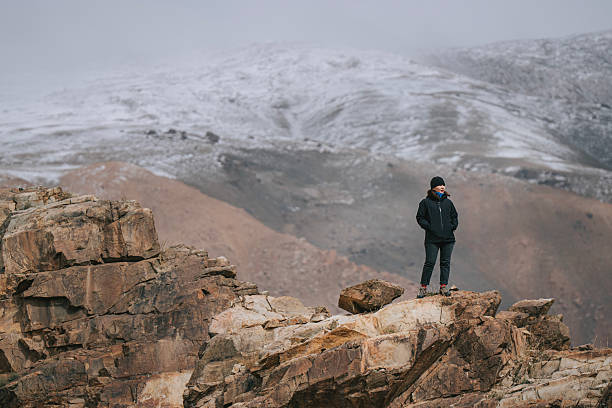 istock Mongolian Woman Standing on Rocky Cliff Overlooking Snow-Covered Mountain 2229194137