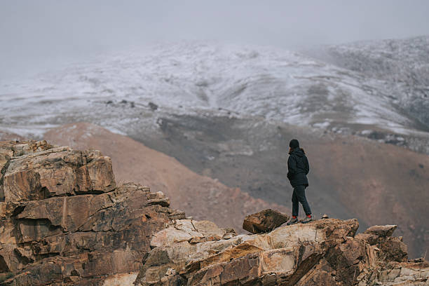 istock Mongolian Woman Standing on Rocky Cliff Overlooking Snow-Covered Mountain 2229194154