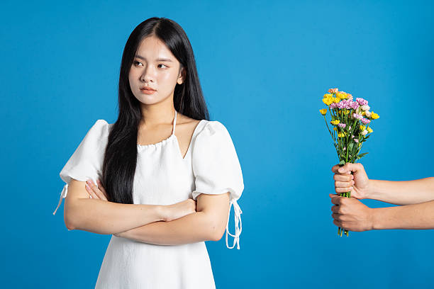 Upset woman refusing flowers offered by someone unseen against a vibrant blue backdrop