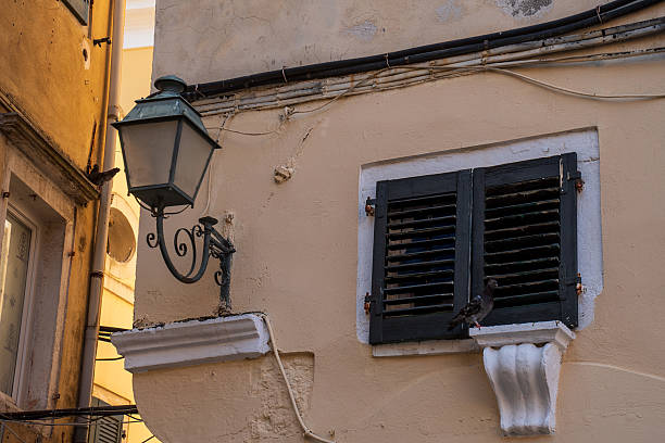 Residential building paint in pastel colour typical for Corfu architecture, green wooden shutters, vintage street light