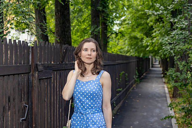 istock Woman in blue polka dot dress walking along tree-lined pathway 2229197224