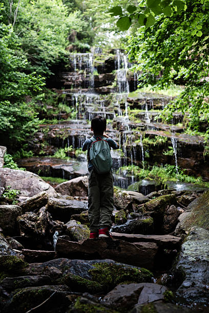 istock Young hiker admiring cascading waterfall in lush forest 2229198260