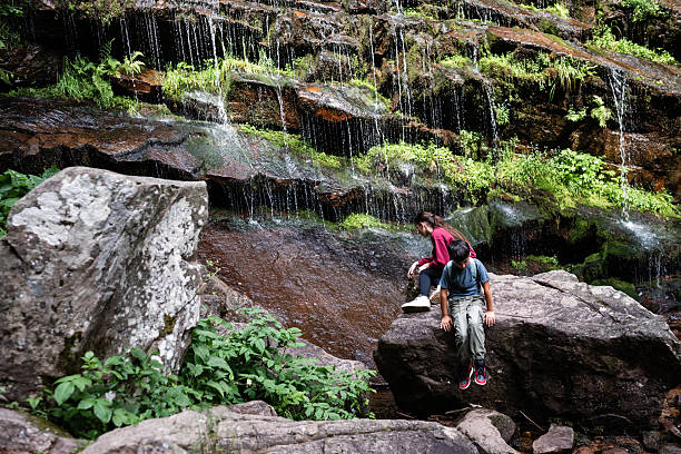istock Hikers resting by waterfall in lush green forest 2229198642