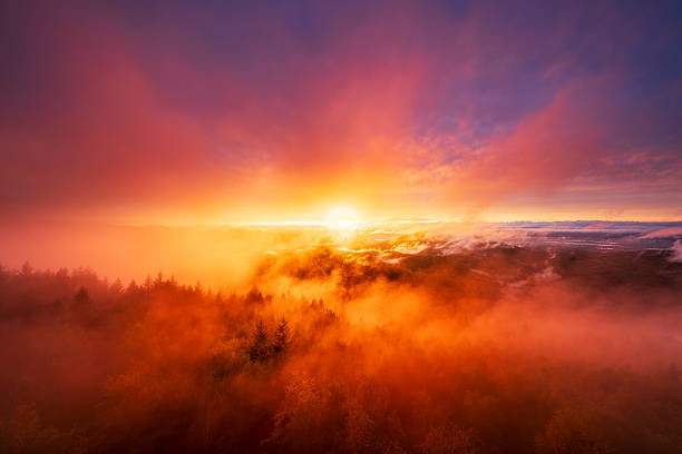 An incredible sunset paints the sky with fiery red and orange hues over the Murg Valley in Germany's Northern Black Forest. Thick mist fills the valley, creating a dramatic and powerful scene.