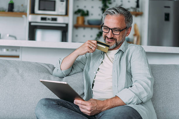 istock Man sitting on the sofa at home and using tablet for online shopping. 2229200382