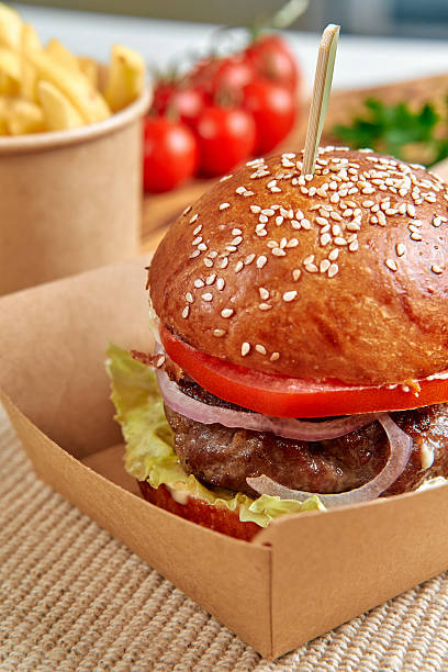 istock Delicious Gourmet Burger with Fresh Lettuce, Tomato, and Onion Nested in a Soft Sesame Seed Bun Accompanied by Crispy French Fries and Garnished with Cherry Tomatoes 2229200488