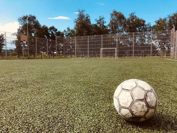 A worn soccer ball rests on green turf under clear skies.