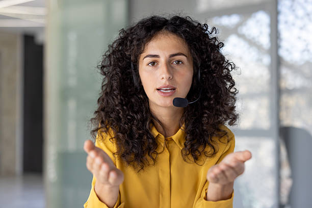 istock A smiling woman wearing a headset speaks directly to the viewer while gesturing with her hands. 2229201740