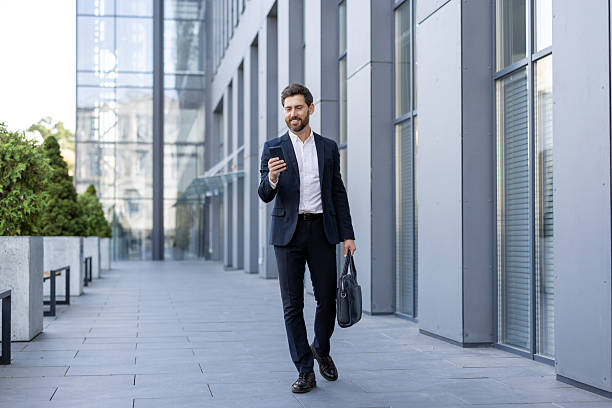 istock A smiling businessman in a suit walks while looking at his smartphone in an urban setting. 2229206580