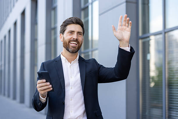 istock A smiling businessman waves while holding his smartphone, looking happy and successful. 2229206630