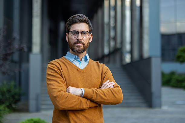 istock An attractive man with glasses confidently stands outside a modern office building with arms crossed. 2229206705