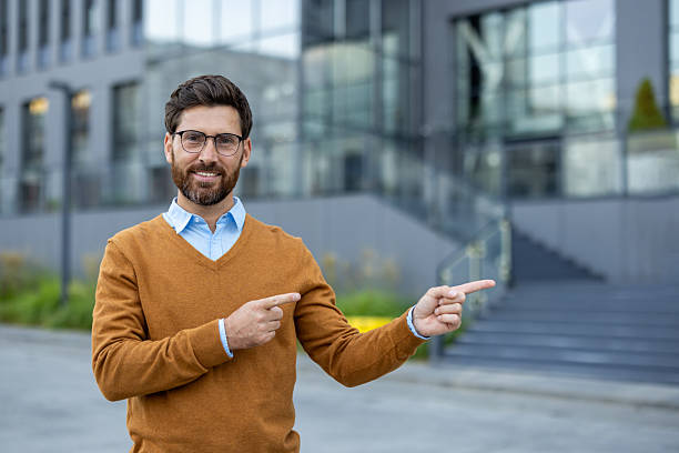 istock A smiling man points to the side, set against a modern office building background. 2229206709