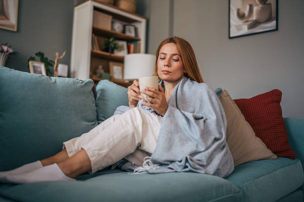 istock Woman relaxing on sofa with warm drink and cozy blanket 2229208023