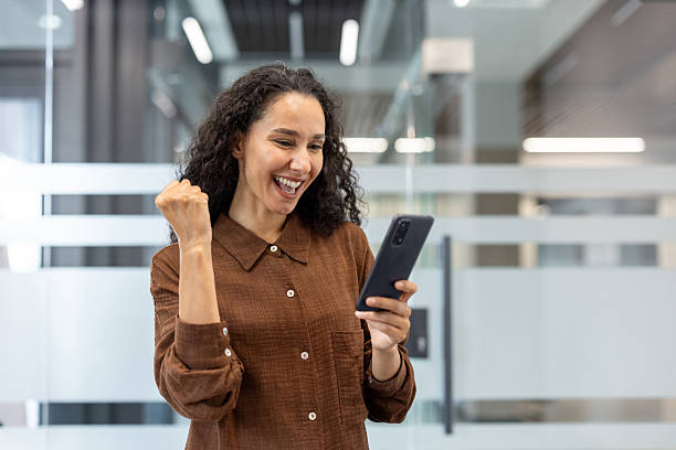 istock A woman reacts with excitement while looking at her phone in an office setting. 2229220247