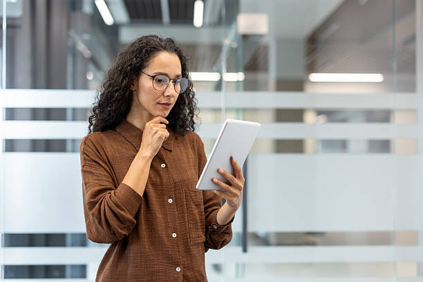 istock A woman in glasses thoughtfully examines a tablet screen in a modern office environment. 2229220261
