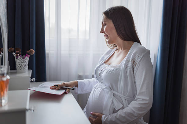 Pregnant woman writing in notebook at home