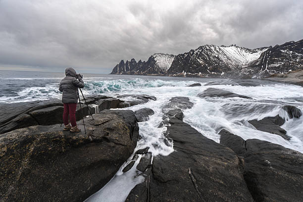 A lady standing and taking a photo on the edge of rock at Tungeneset coastline,Devil's teeth,Okshornan Range,Senja,Troms,Norway.