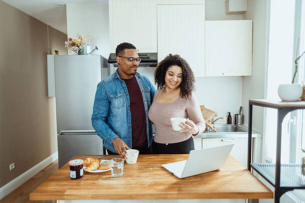 istock Multiracial heterosexual couple at home drinking coffee and using laptop at kitchen counter 2229237423