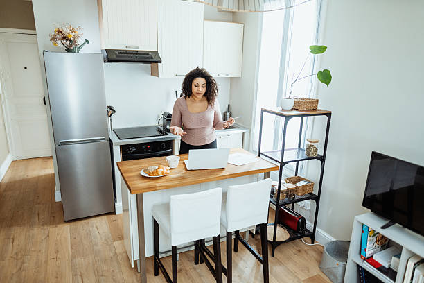 istock Single woman working at home on kitchen counter, using laptop, phone and digital tablet while enjoying coffee 2229237831