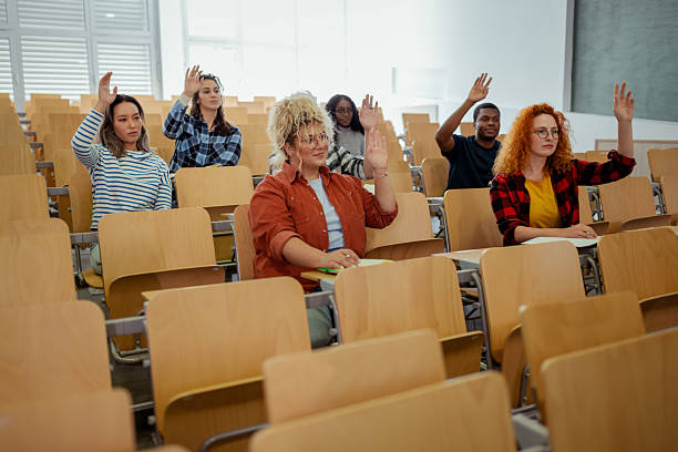 istock Multiethnic group of college students raising hands to answer question during a auditorium classroom 2229260118
