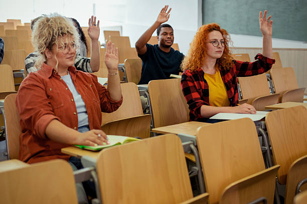 istock Multiethnic group of college students raising hands to answer question during a auditorium classroom 2229260179