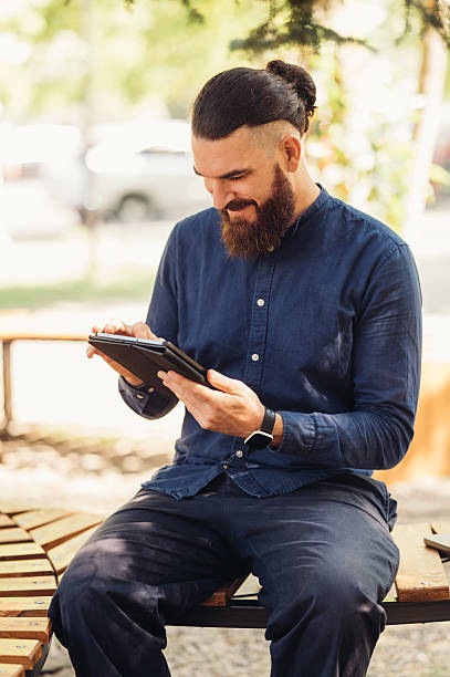istock A man is actively engaging with his tablet while sitting outdoors in a public park setting 2229272845