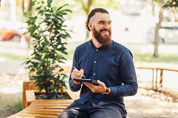 A Smiling Man Engaging with a Tablet While Sitting in an Outdoor Urban Environment