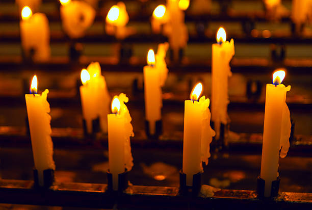 Warm candlelight flickers softly on multiple wax candles arranged in rows, creating a serene and contemplative atmosphere. Glowing candle flames evoke feelings of peace, reflection and calm
