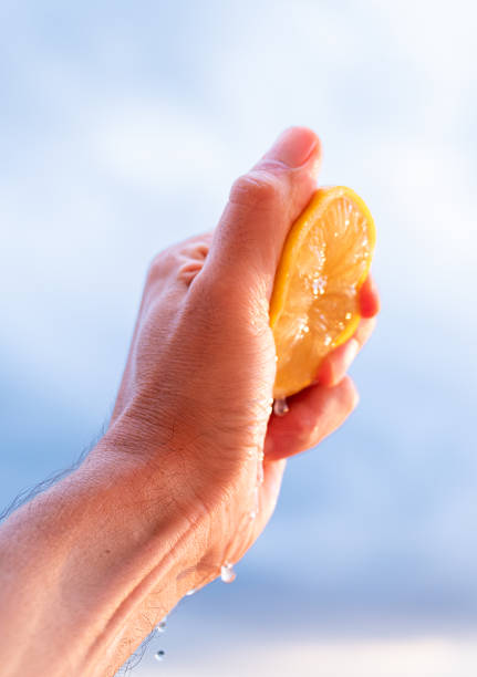 istock Hand squeezing lemon slice with juice dripping at sunset 2229280631