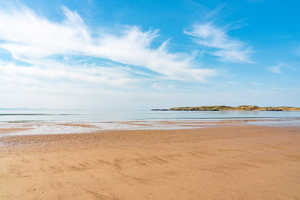 Scenic view of the beach at low tide with llanddwyn island in the background, under a beautiful cloudy sky