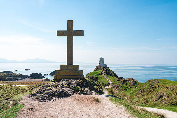 Scenic view of twr mawr lighthouse with a stone cross in the foreground on llanddwyn island, anglesey, wales