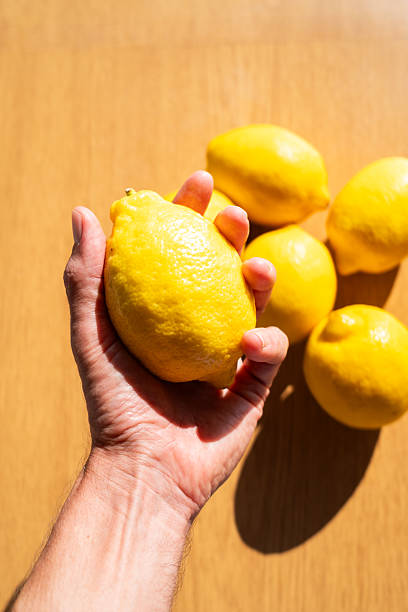 istock Hand holding a fresh ripe lemon with more lemons on a wooden table 2229281372
