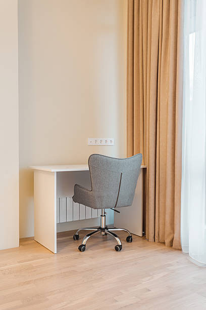 istock Modern workspace with a gray chair and simple desk in a well-lit room featuring soft curtains and light wooden flooring 2229285716