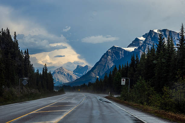 Car driving along Icefields Parkway toward towering Rocky Mountains