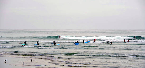 Surfer in wetsuit holding surfboard stands in the ocean with gentle waves under an overcast sky