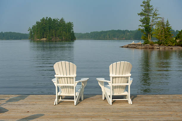 istock Chairs on a dock facing a wooded island across a still lake 2229290131