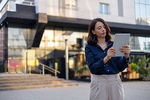 istock Businesswoman using a digital tablet while standing in front of a sleek, modern office building, embodying professionalism in an urban setting 2229295617
