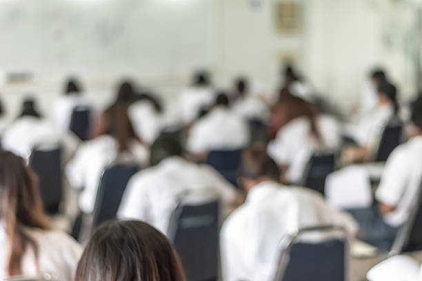 istock Blur school student exam background in university class with blurry view from back of the classroom of young people having stress doing examination admission test in classroom for education 2229300090