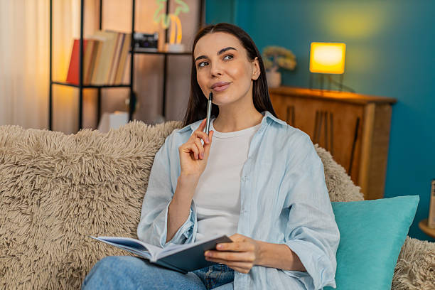 istock Young woman on sofa carefully writing notes in notebook thoughtfully making important todo list 2229303434