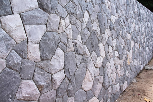The image displays a close-up of a traditional Danish rock wall constructed with round stones, some of which have moss growth. The wall showcases natural textures, shapes, and harmonious earthy tones.